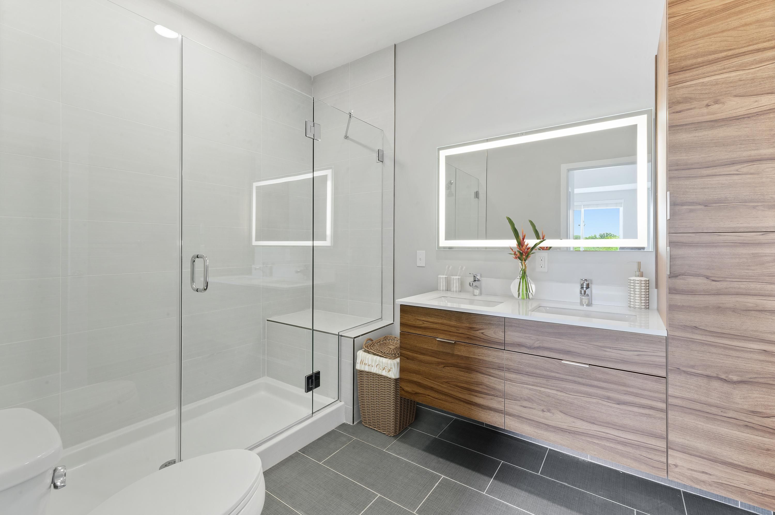 Modern bathroom with a glass shower, wood vanity, and illuminated mirror.