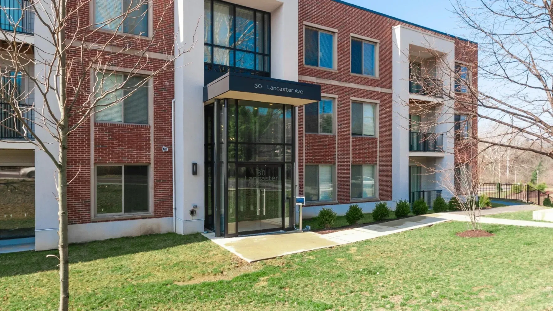 Modern brick apartment building entrance with large glass doors and greenery.