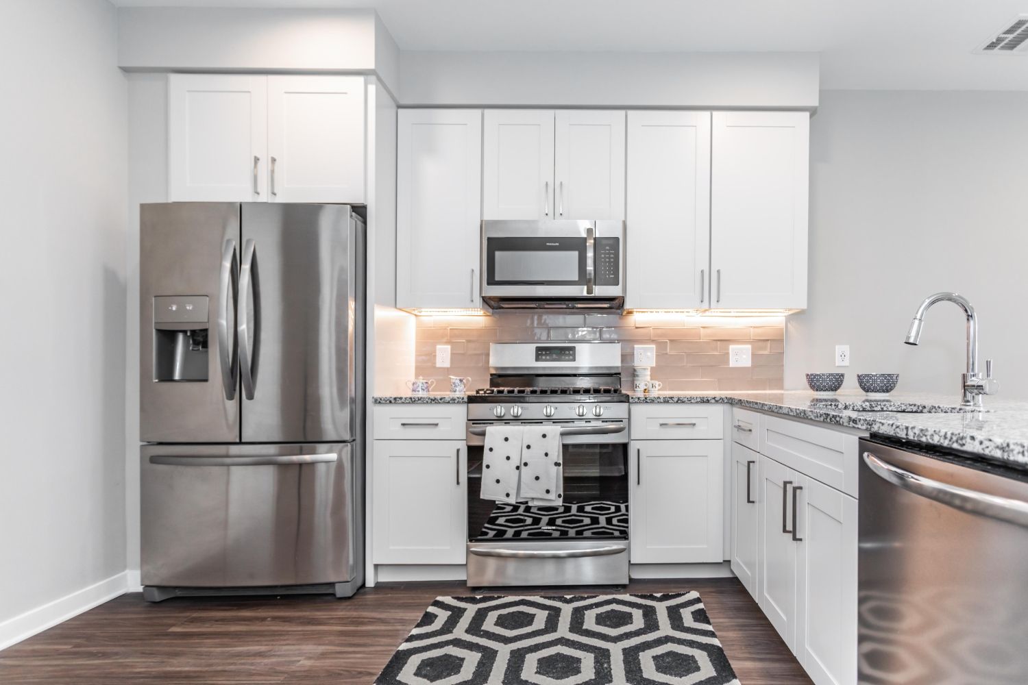 Modern kitchen with stainless steel appliances, white cabinets, and patterned rug.