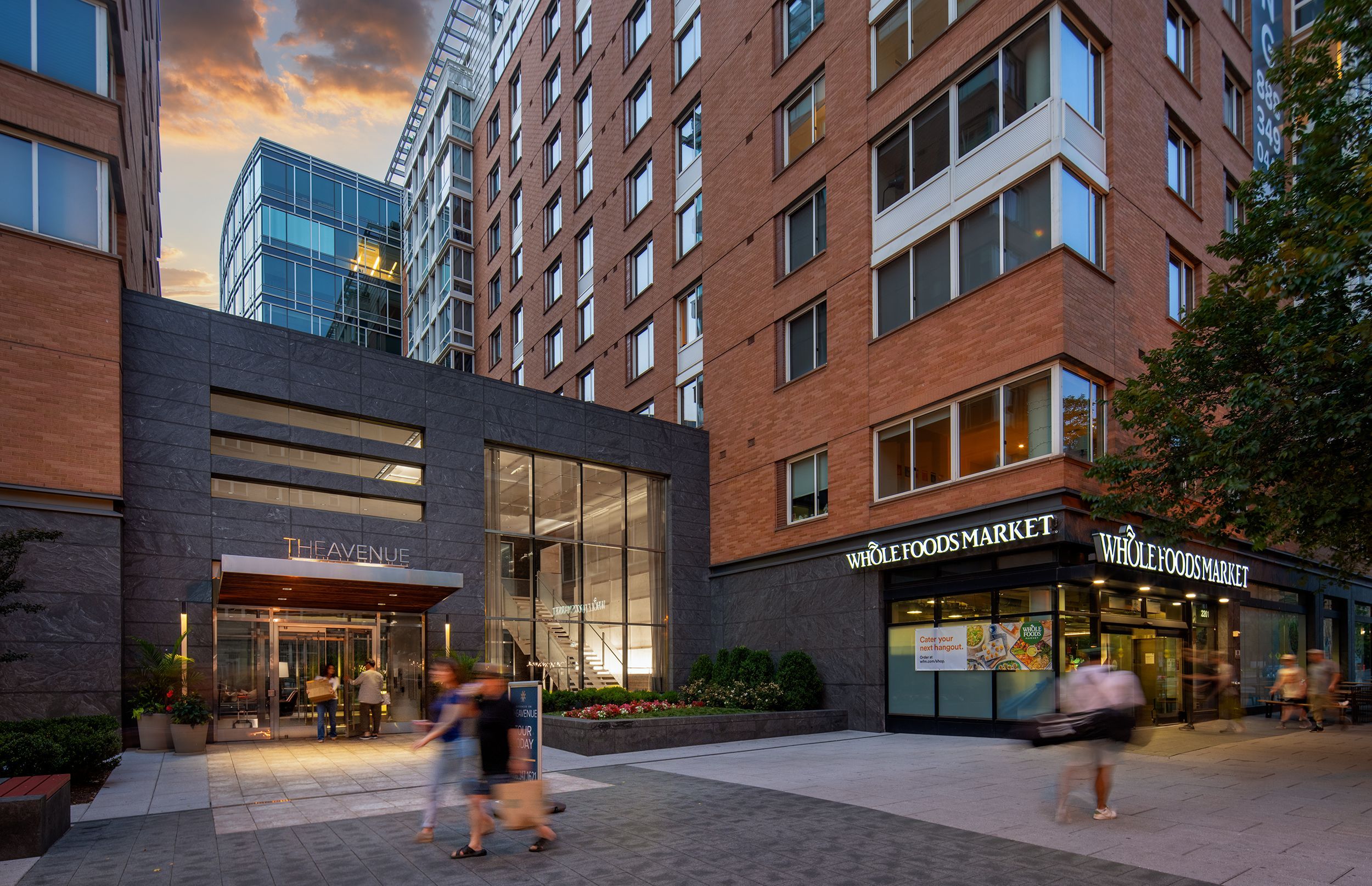 Modern building with glass entrance and restaurant, surrounded by people at sunset.