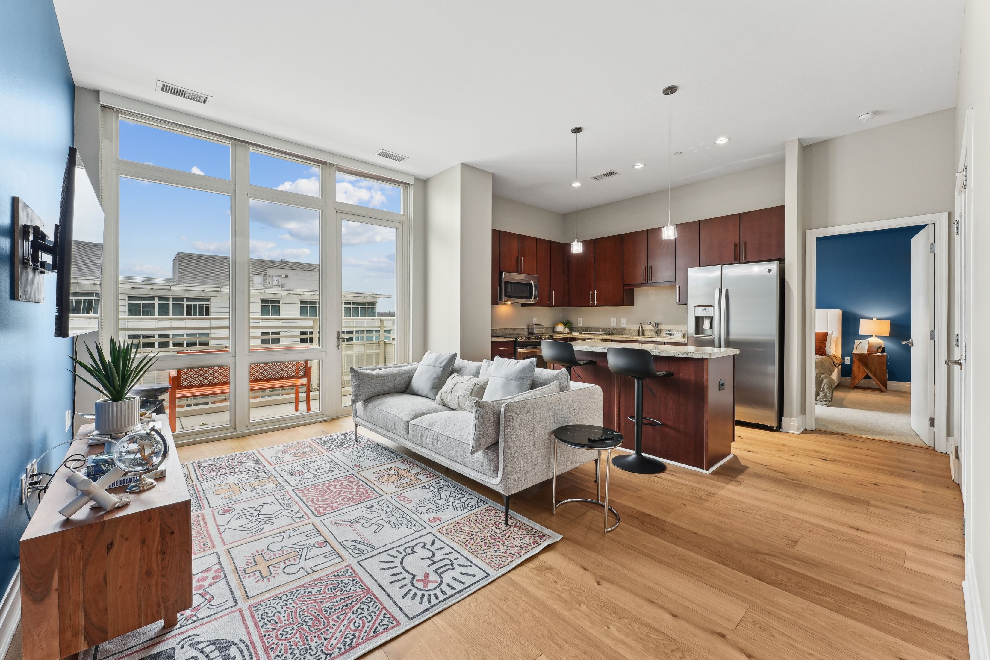Modern apartment living space with a kitchen, sofa, and large windows offering outdoor views.