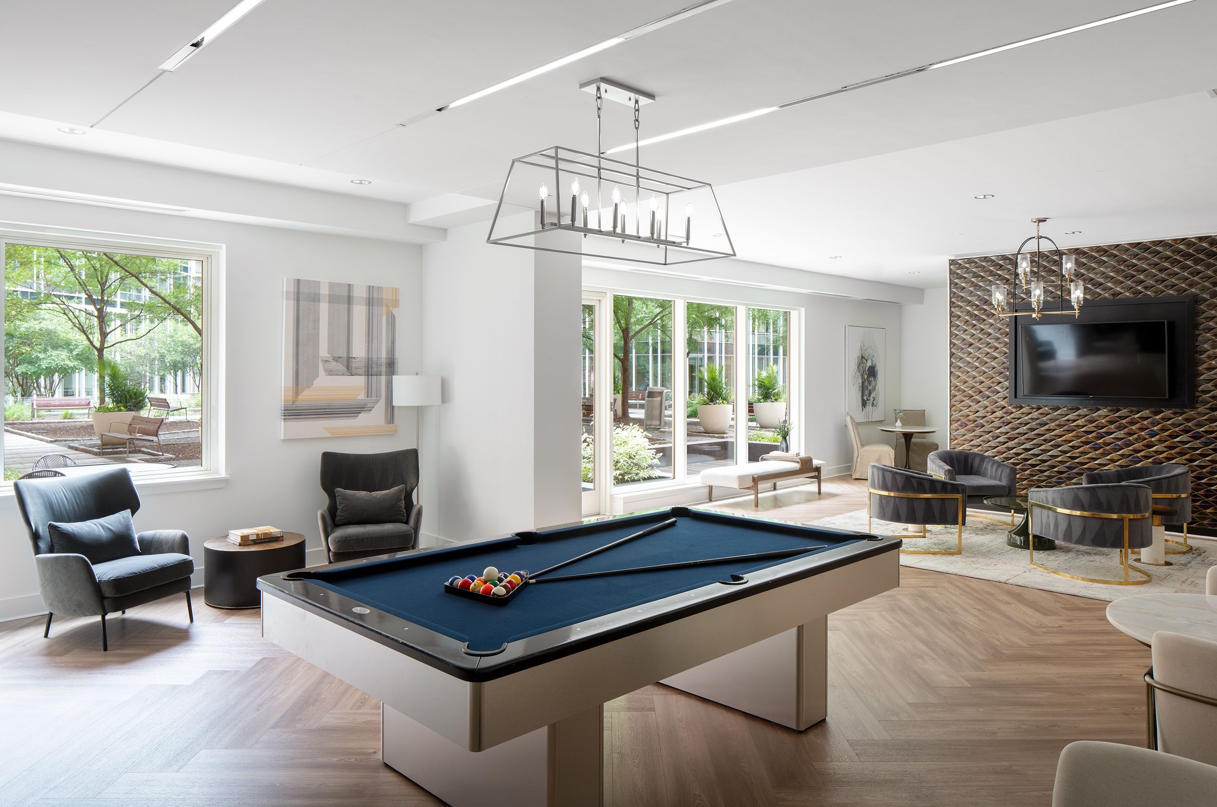 Modern lounge with a pool table and large windows overlooking greenery.