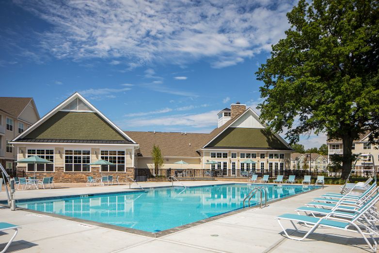 Outdoor swimming pool with lounge chairs and a clubhouse against a partly cloudy sky.