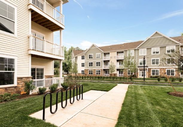 Two apartment buildings alongside a grassy area with a walking path and bike racks.