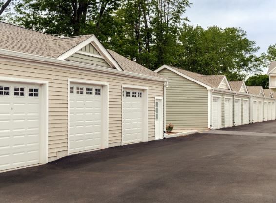 Row of beige garages with individual doors in a paved area, surrounded by greenery.
