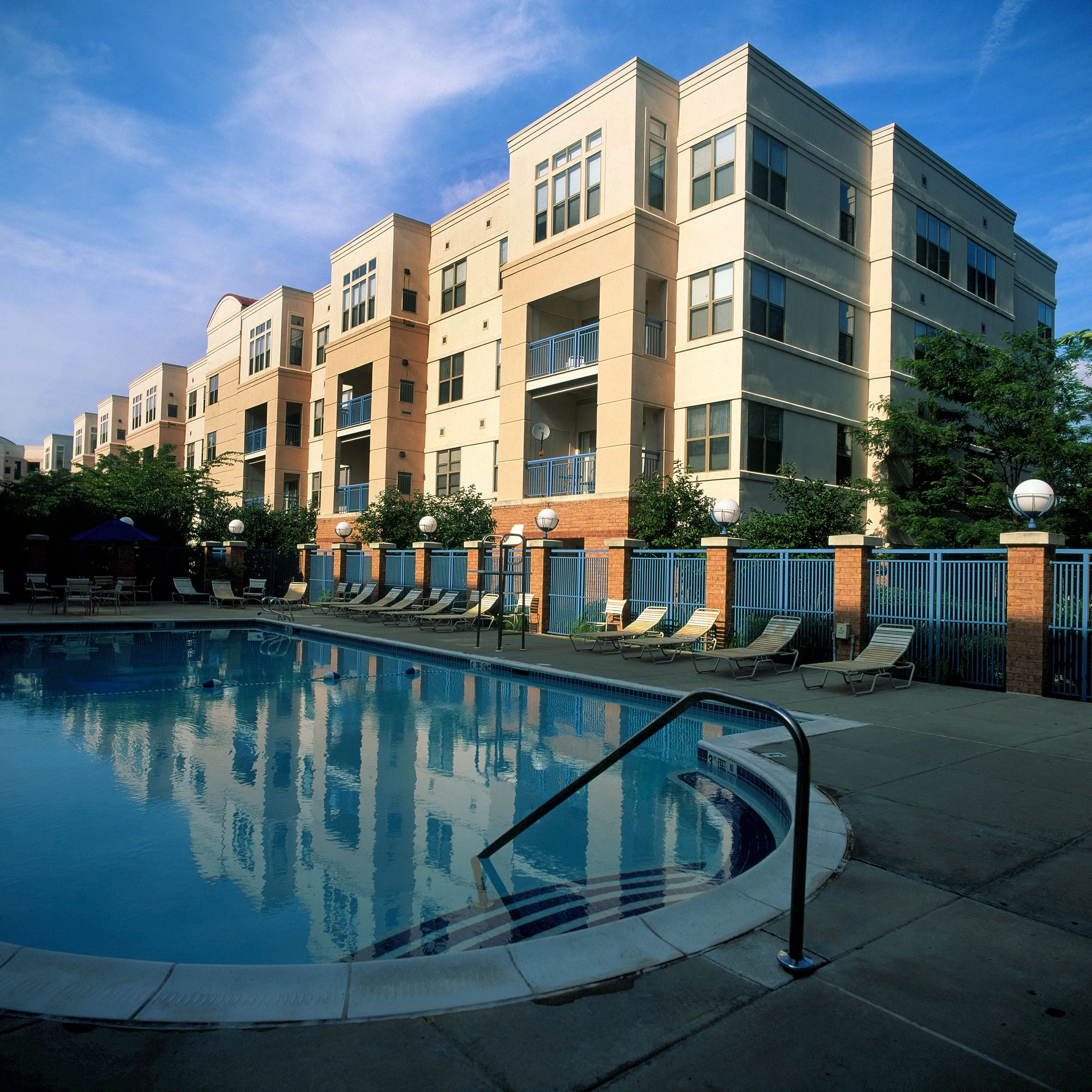 Modern apartment buildings beside a clear swimming pool under a blue sky.