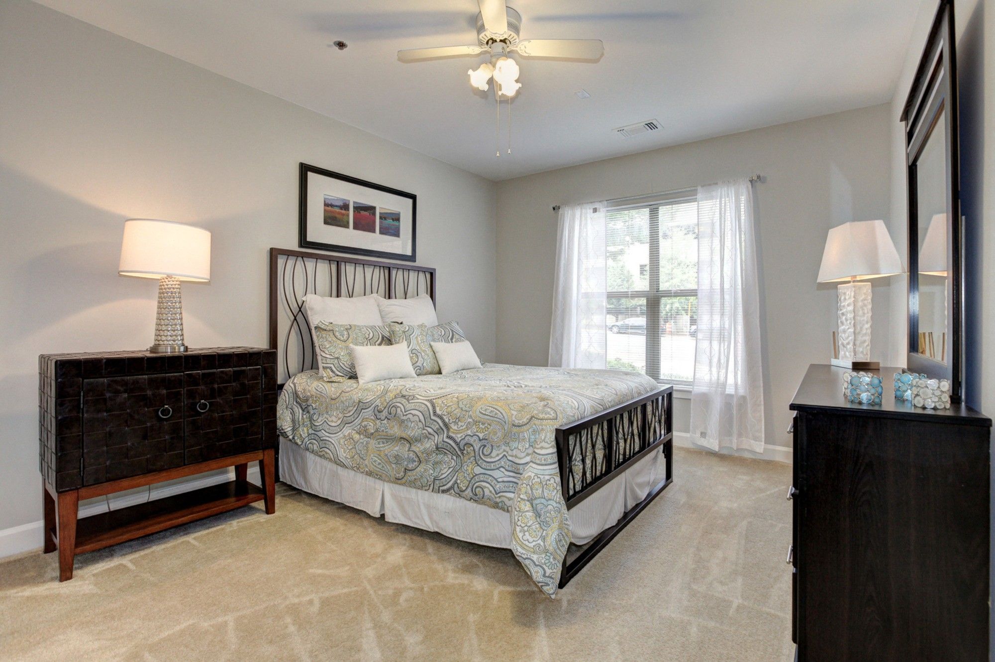 Cozy bedroom with a queen bed, nightstand, dresser, and natural light from a window.
