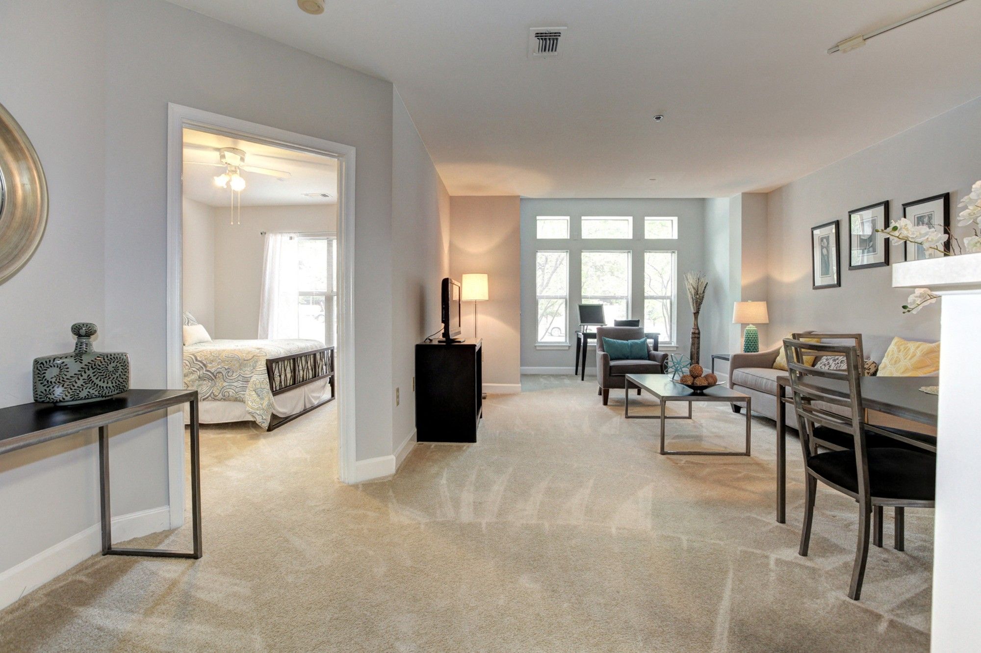 Bright, modern living space with a desk, seating area, and a glimpse of a bedroom.