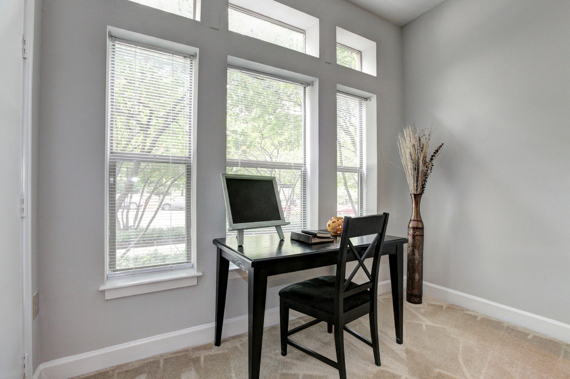 A minimalist workspace with a black chair and desk in a light-filled room by large windows.