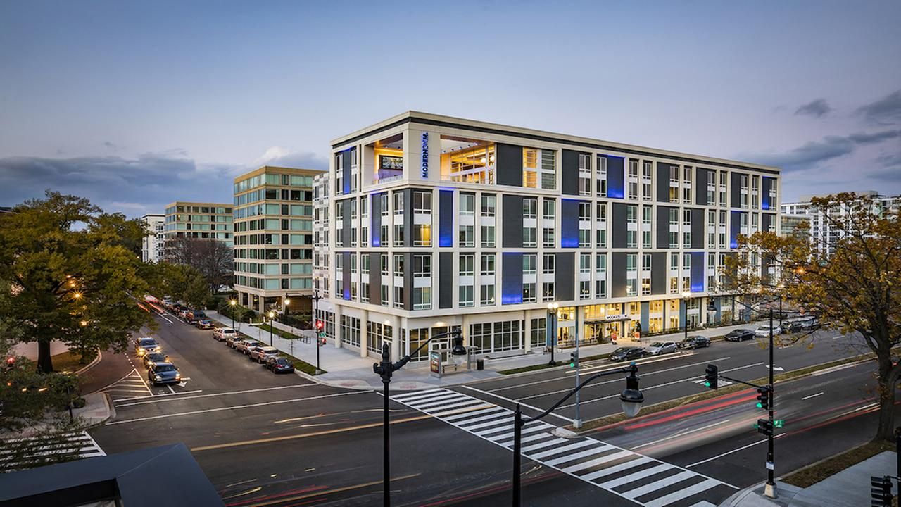 Modern multi-story building with a mix of blue and gray accents, set in an urban landscape.
