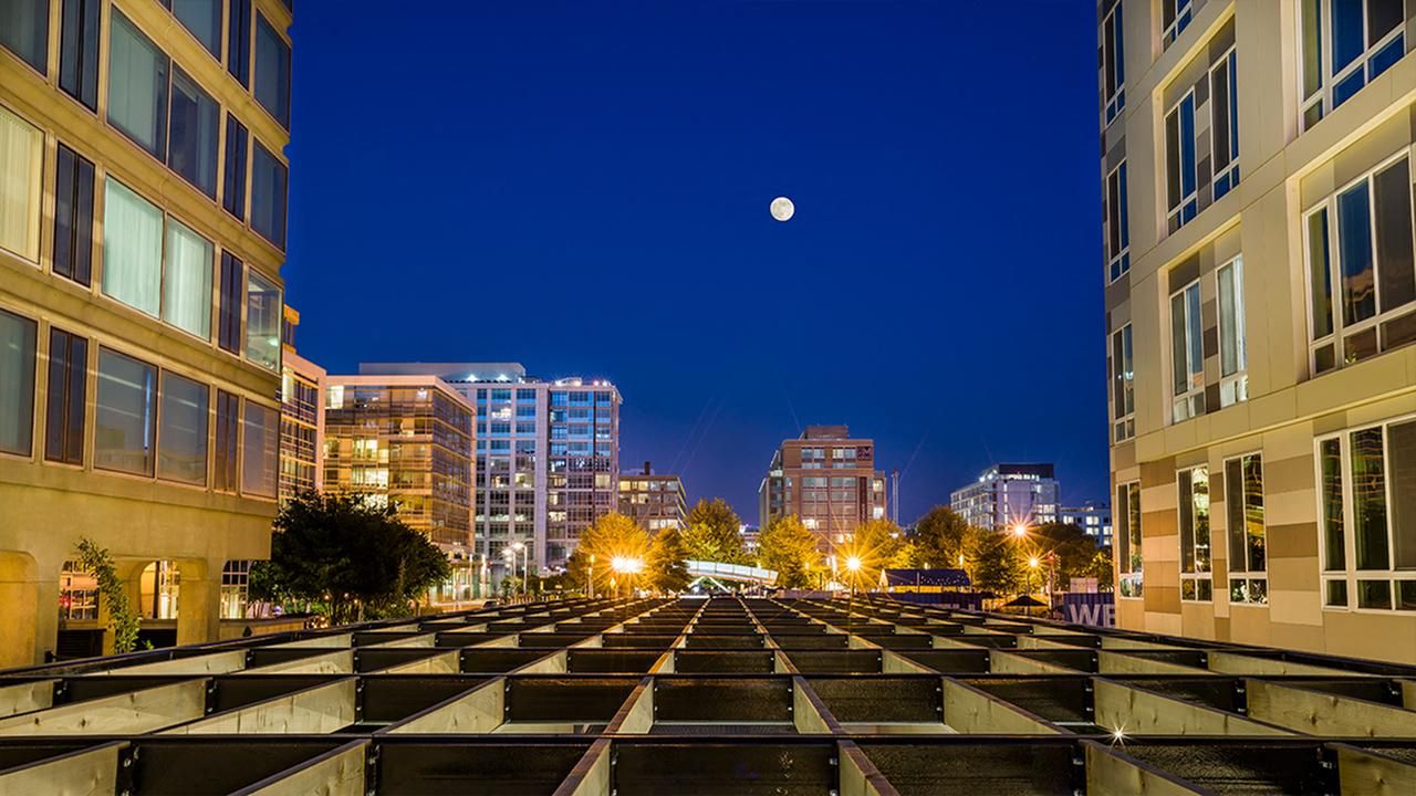 Night scene of a city skyline under a bright moon with illuminated buildings.