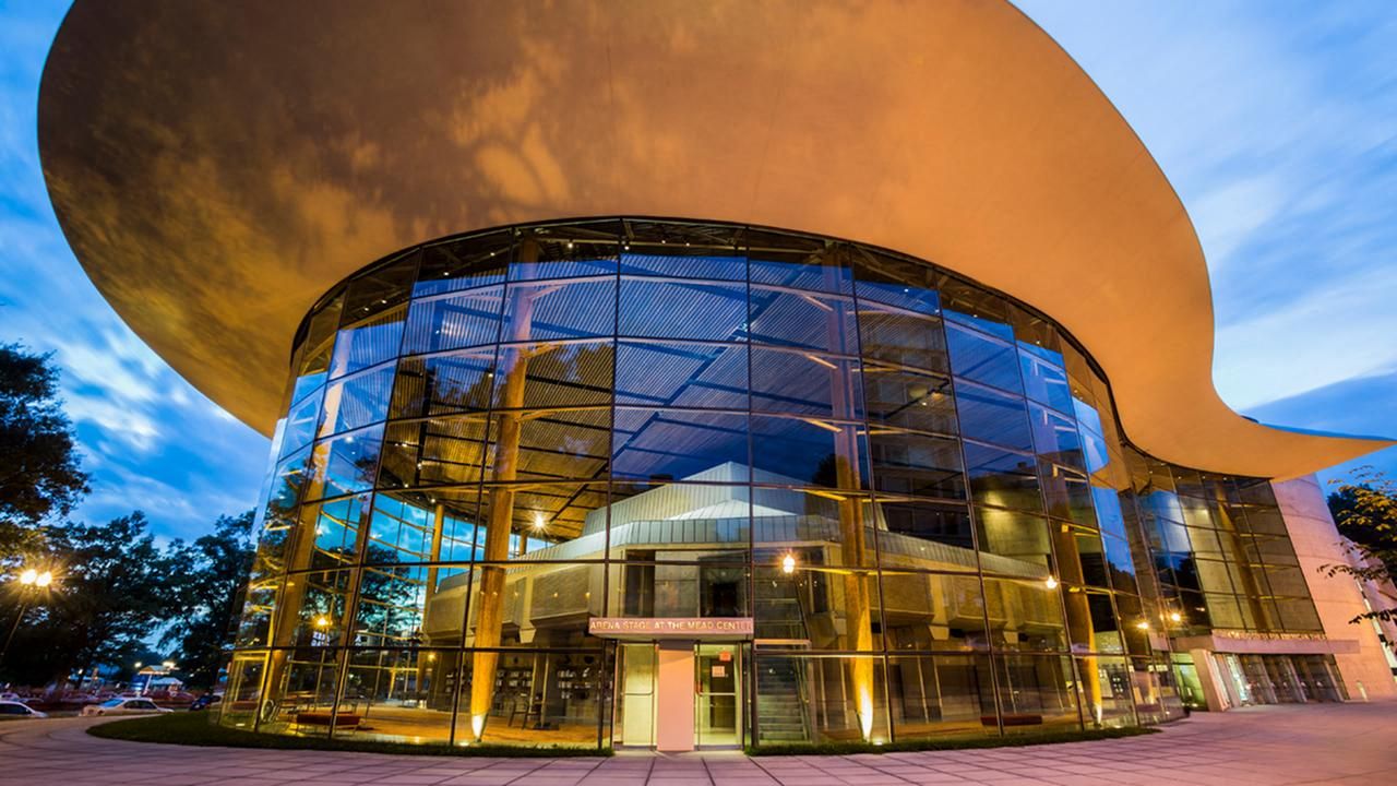 Modern glass building with a large, curved roof against a twilight sky.