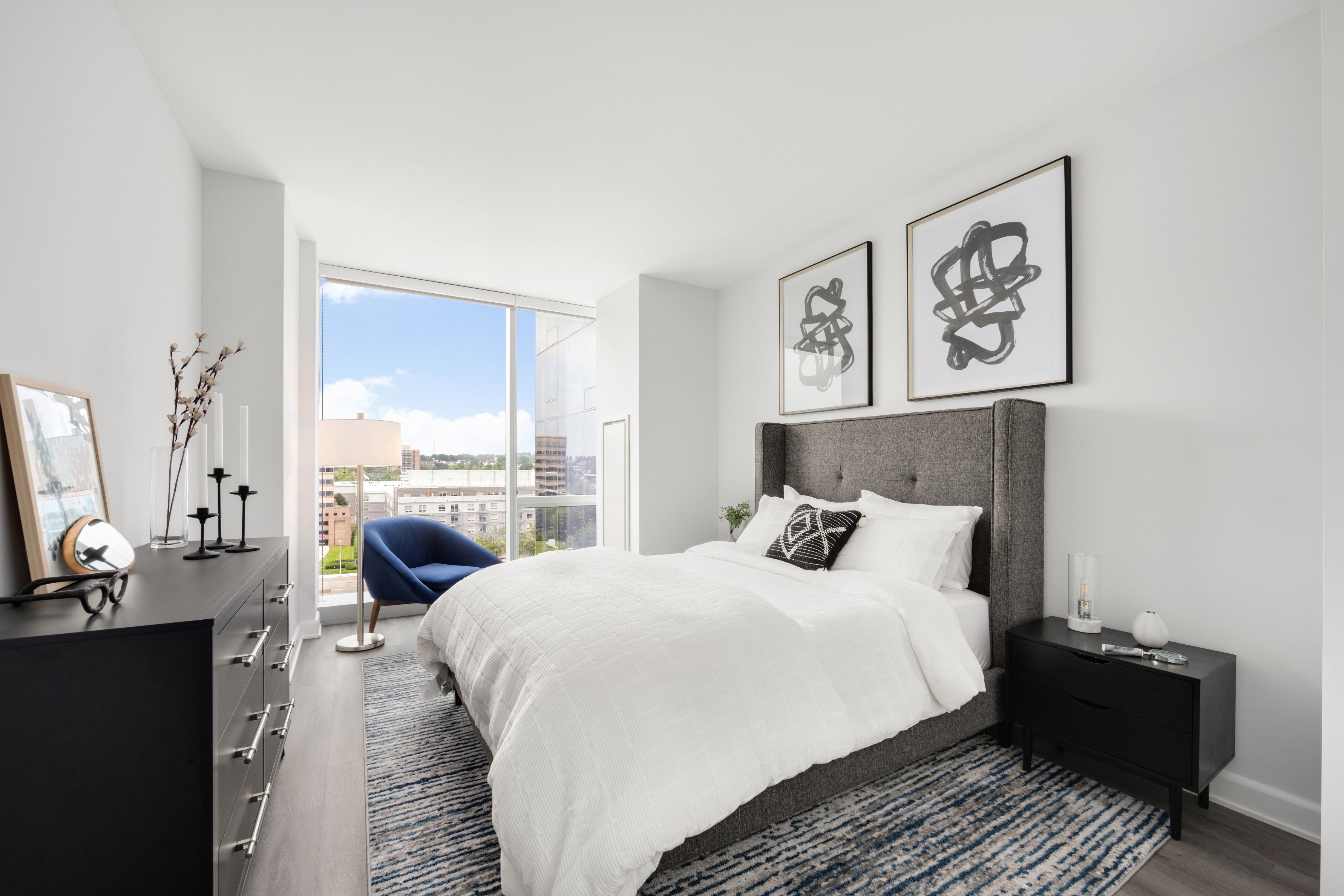 Modern bedroom with a bed, abstract art, and large windows letting in natural light.