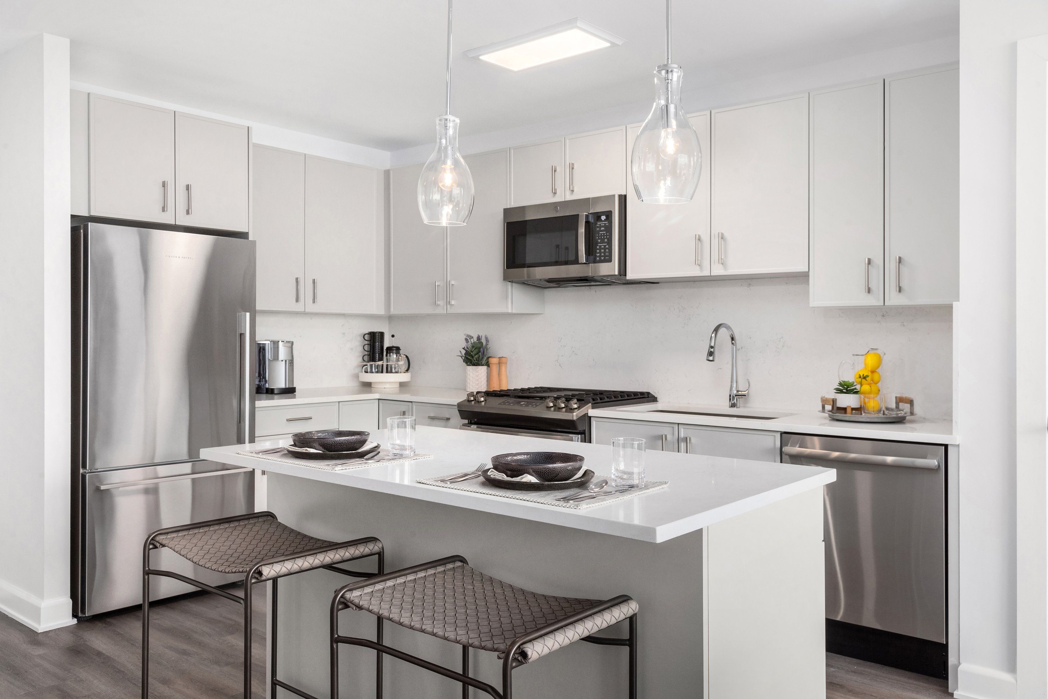 Modern kitchen with stainless steel appliances and a white island bar with two stools.