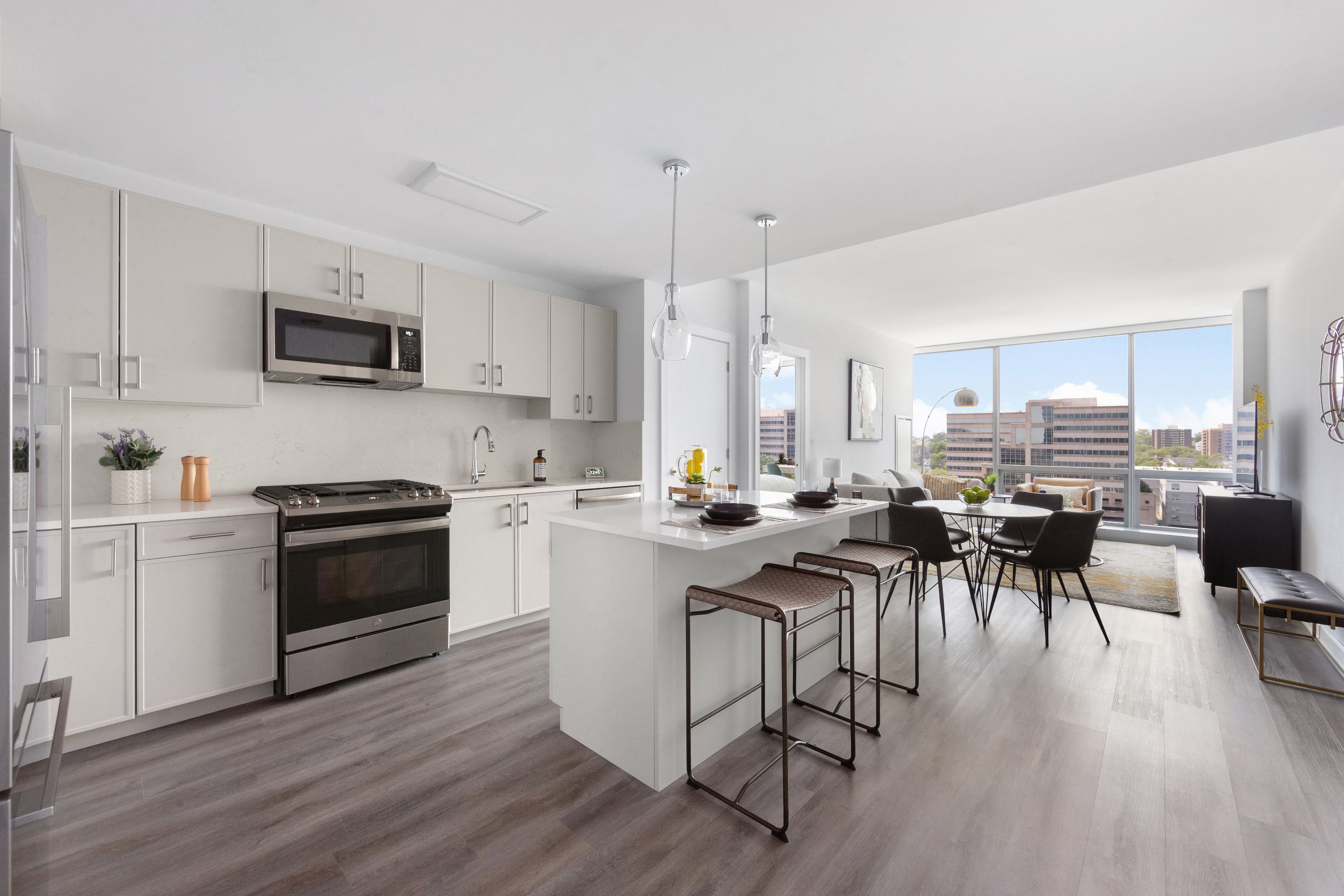 Modern kitchen with white cabinetry, stainless steel appliances, and a dining area by a large window.