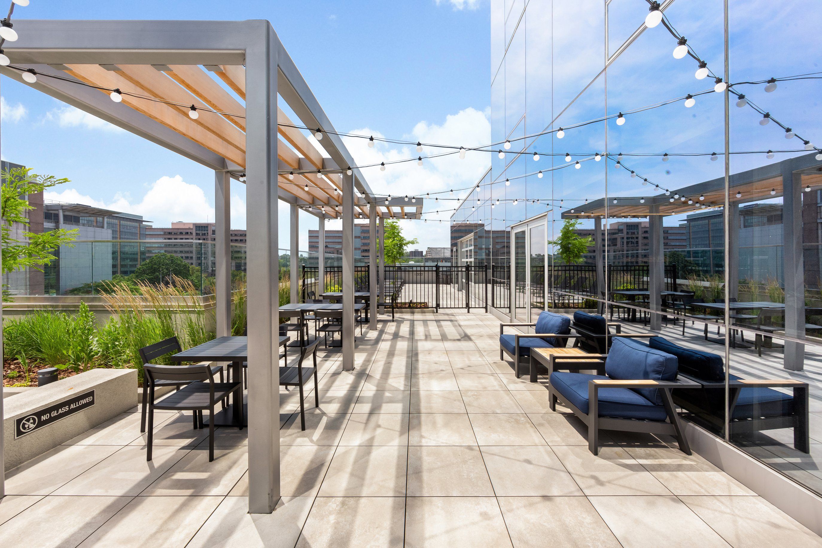 Rooftop patio with seating, decorative lights, and a view of greenery and buildings.