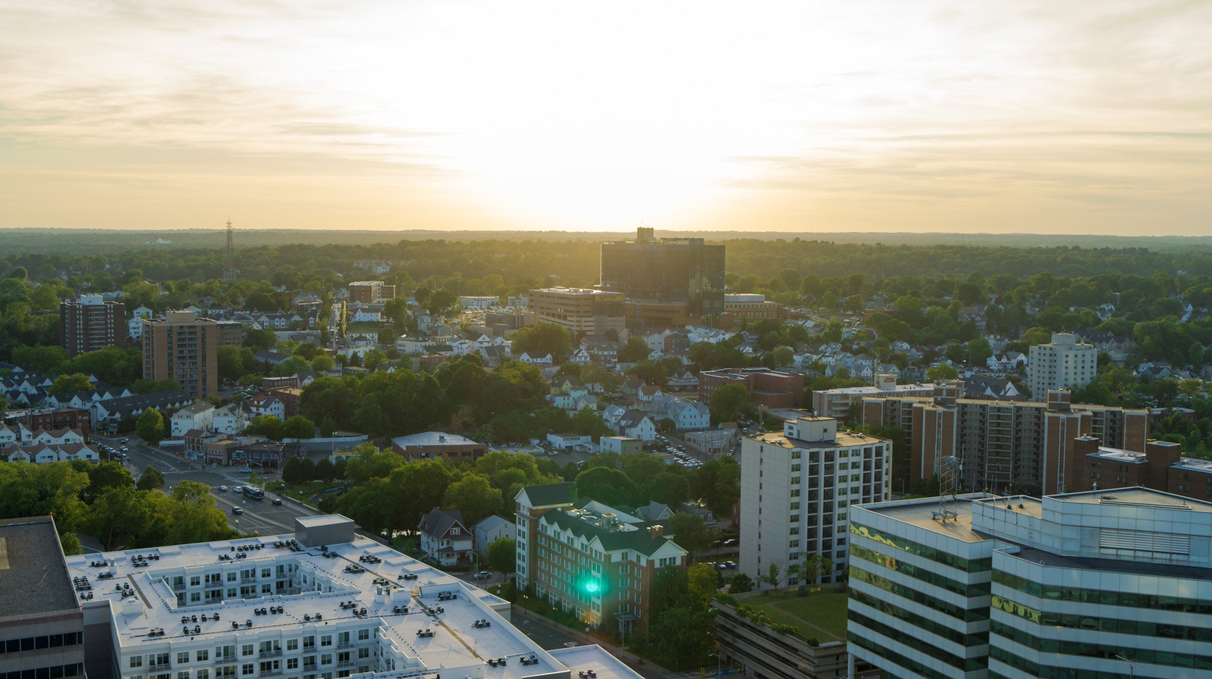 Aerial view of a city skyline at sunset, with buildings and greenery visible.