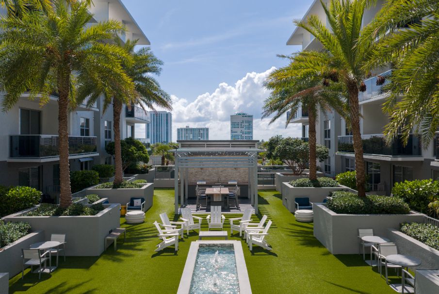 Luxurious outdoor pool area surrounded by palm trees and modern buildings.