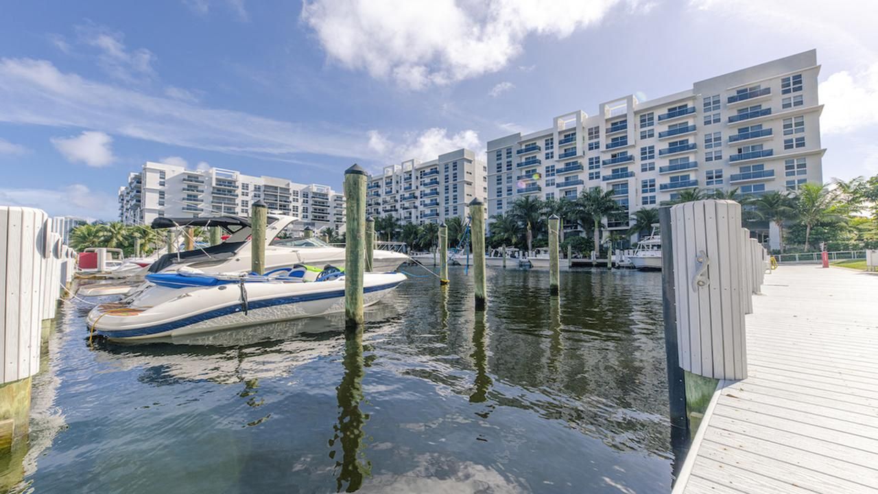 Marina with boats and modern buildings under a blue sky with clouds.