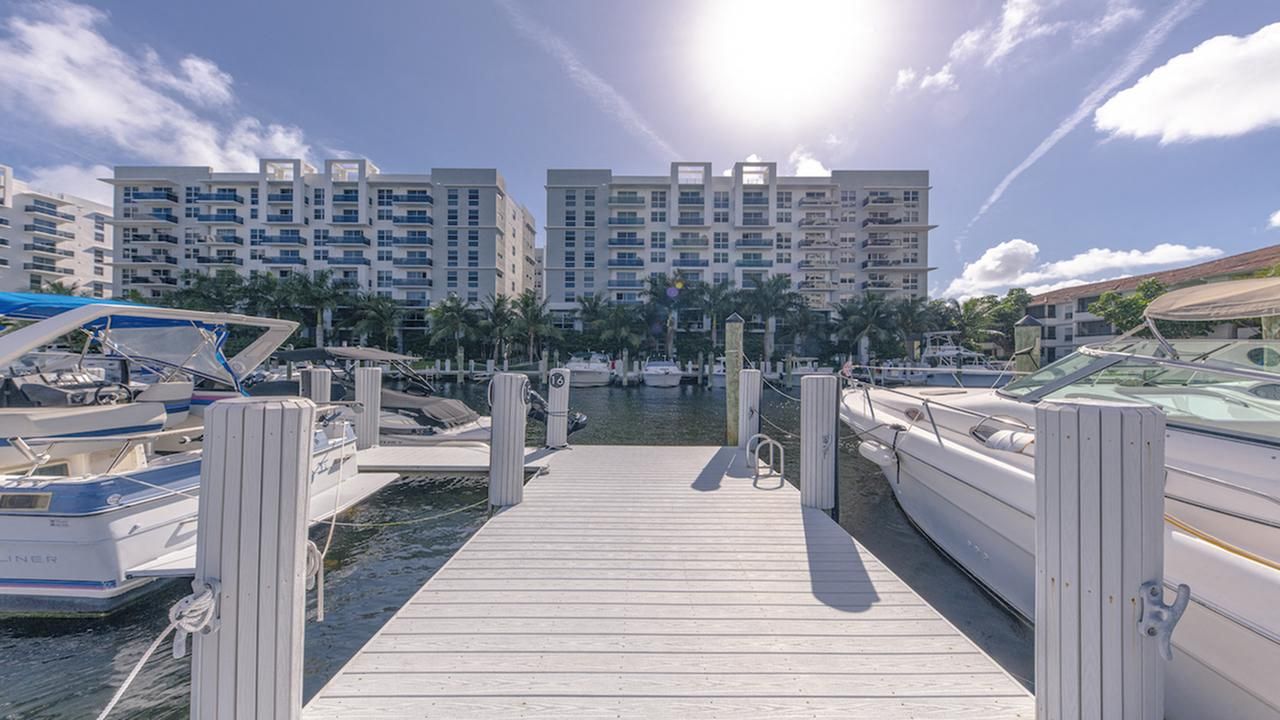 A wooden dock leads to boats and buildings under a bright sun.