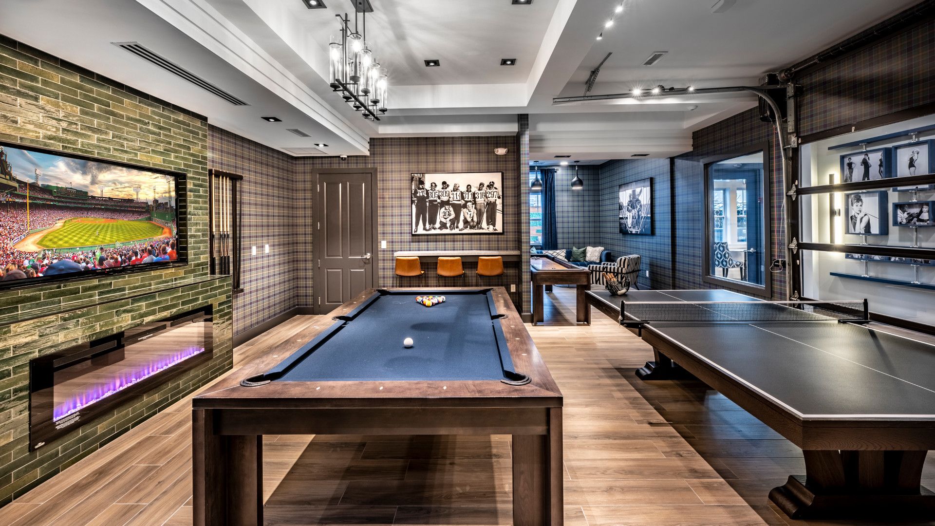 A modern game room featuring a pool table, dartboard, and large screen TV.