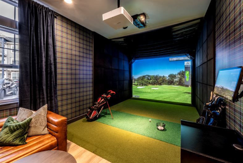 Indoor golf simulator setup with a projection screen, golf clubs, and seating area.