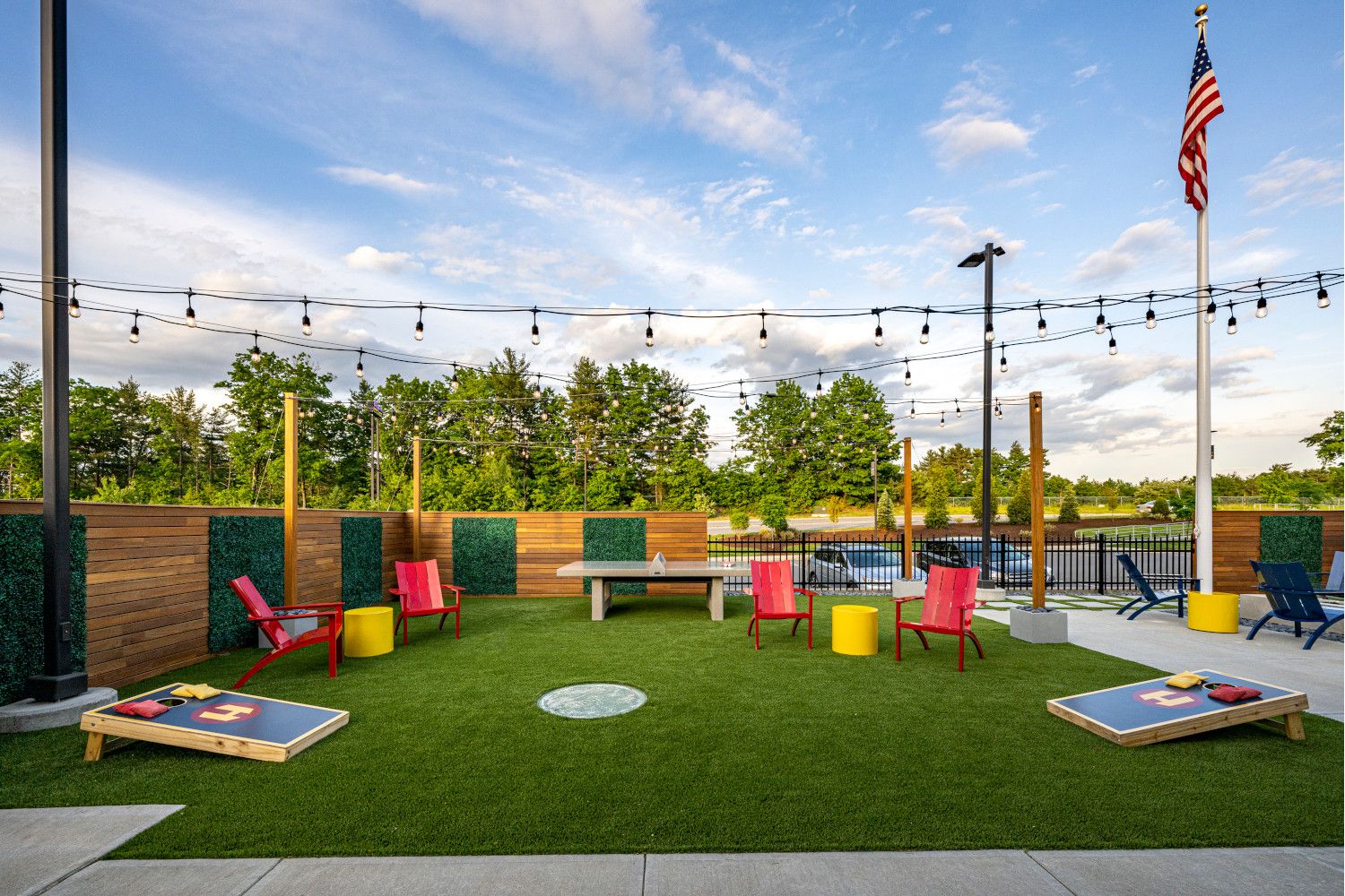 Outdoor lounge area with colorful chairs, green grass, and string lights under a blue sky.