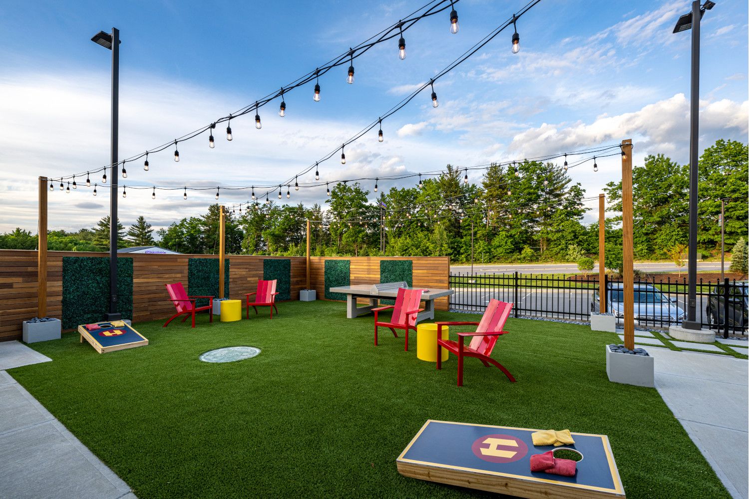 A vibrant outdoor space with lawn, seating, and cornhole games under string lights.