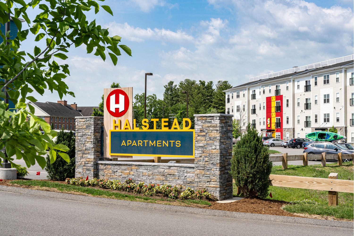 Sign for Hillstead Apartments with a modern building in the background and greenery nearby.
