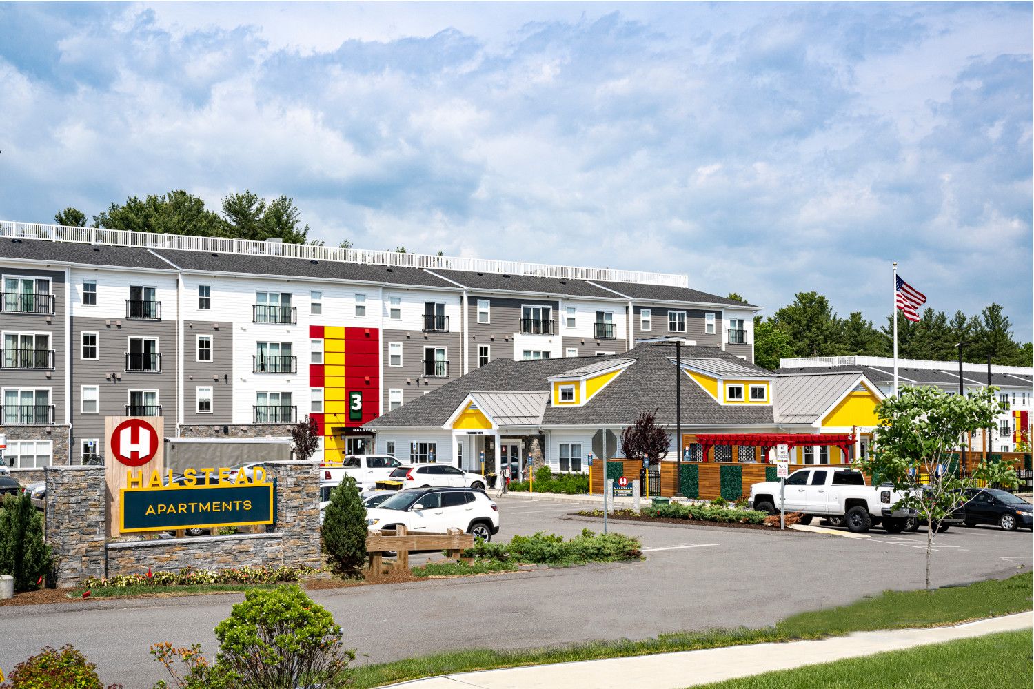 Modern multifamily residential building with landscaped entrance and American flag.