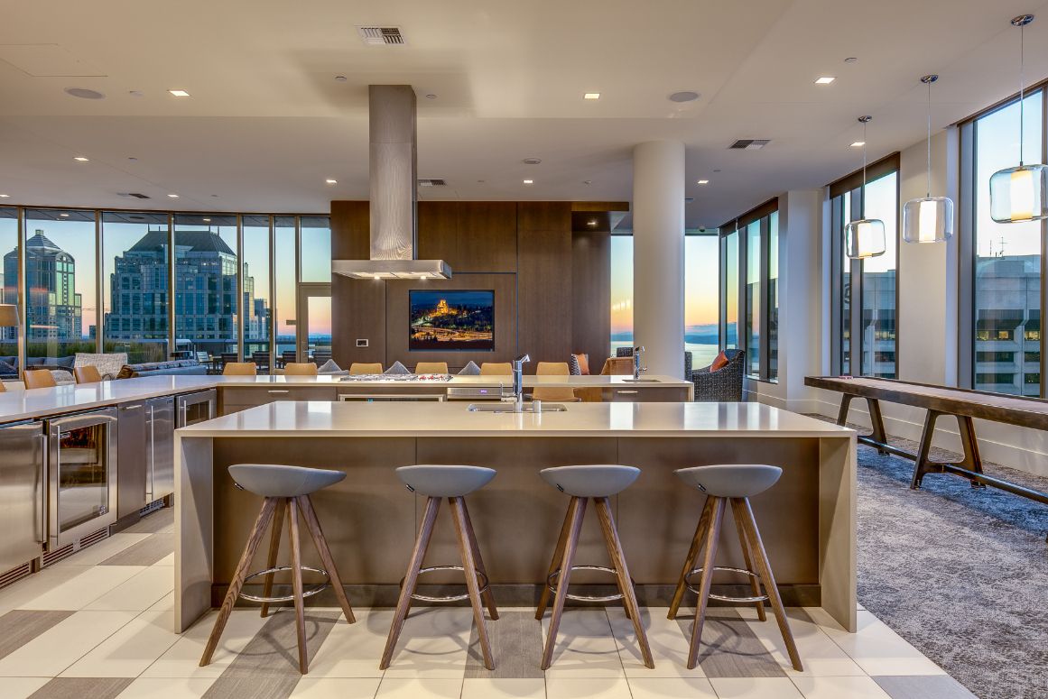Modern kitchen with large island, bar stools, and panoramic city view through large windows.