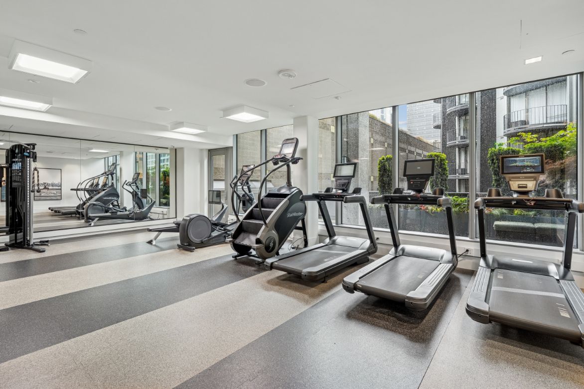 Modern gym with treadmills, an elliptical, and large windows overlooking greenery.