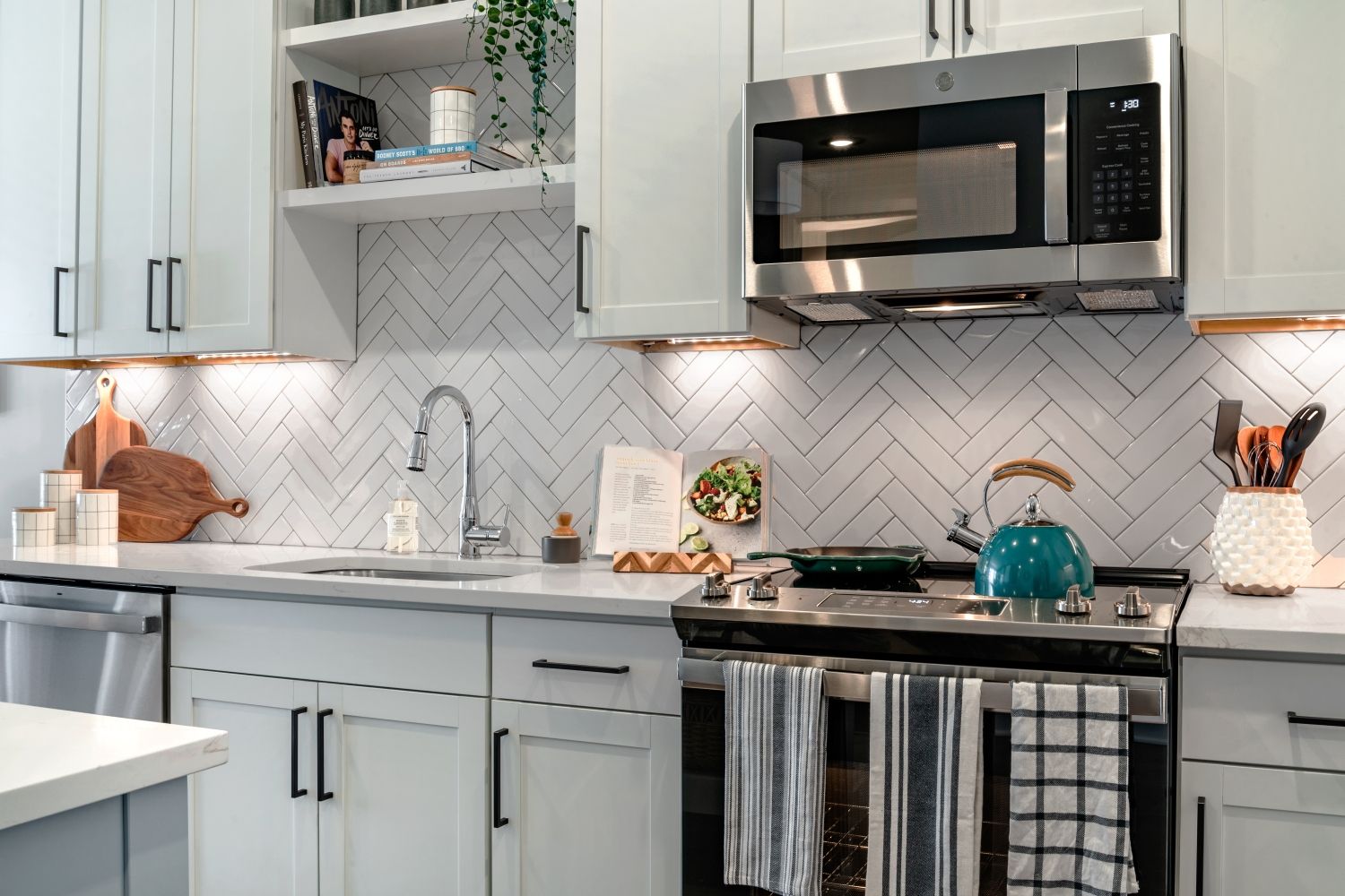 Modern kitchen with white cabinets, herringbone backsplash, and stainless steel appliances.