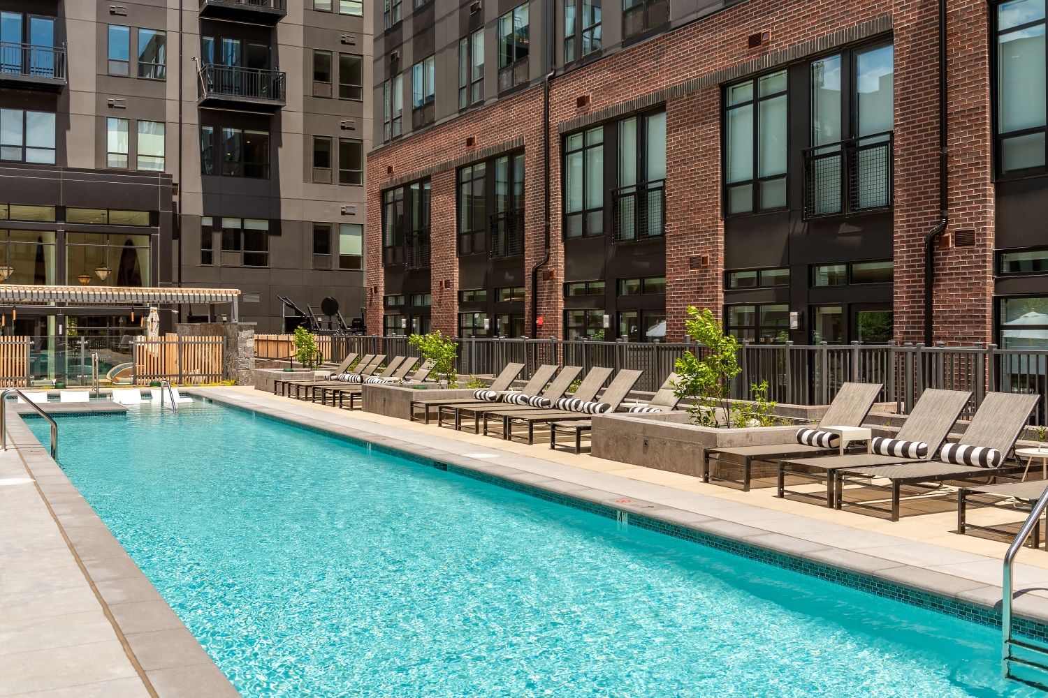 Modern pool area with lounge chairs surrounded by brick buildings.