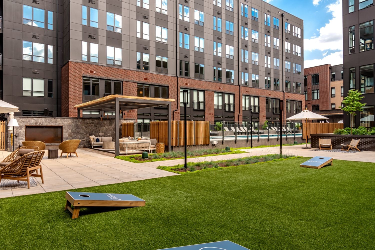 Modern outdoor residential area with green lawn, seating, and a poolside.