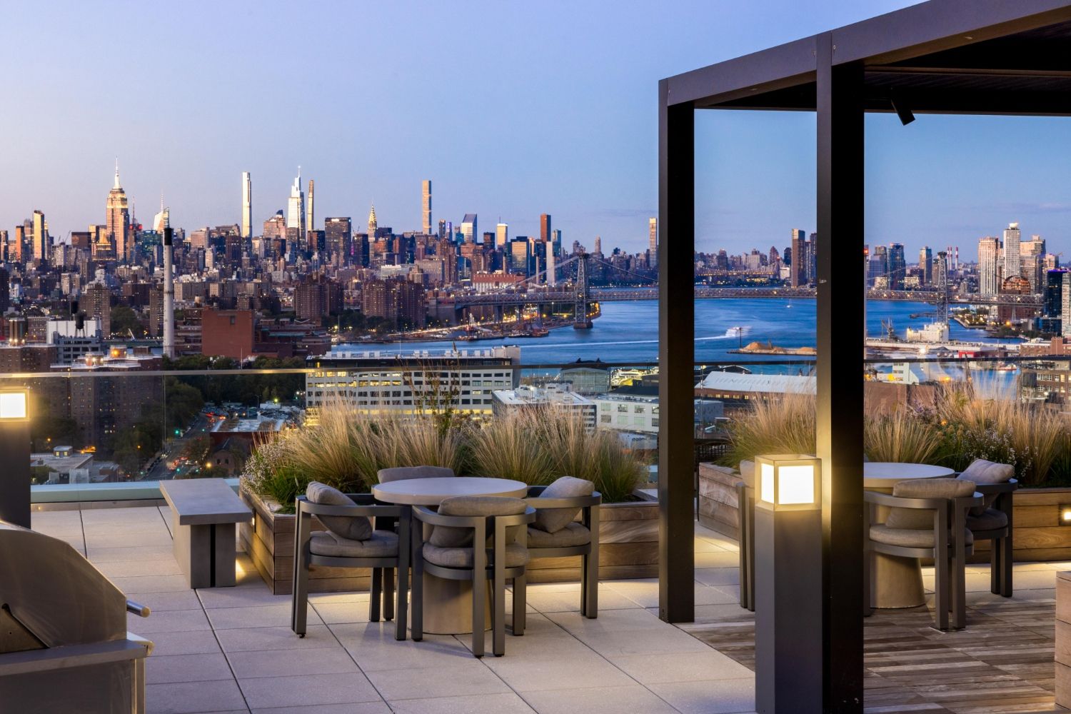 Rooftop terrace overlooking a city skyline at dusk with modern seating and plants.