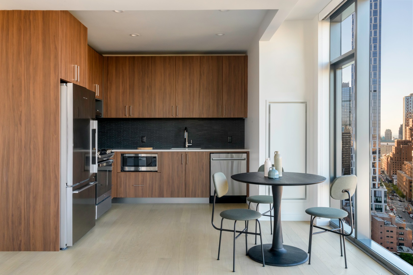 Modern kitchen with wood cabinets, stainless appliances, and a small dining table by a large window.