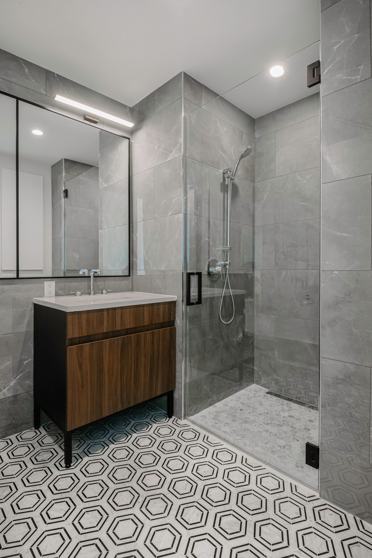 Modern bathroom with gray tiles, wood vanity, and a glass shower.