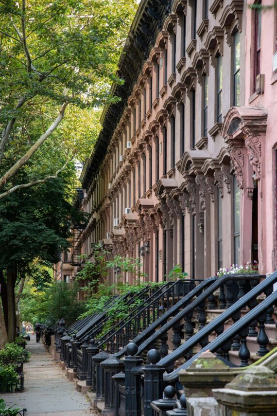 Row of colorful brownstone buildings along a tree-lined street.