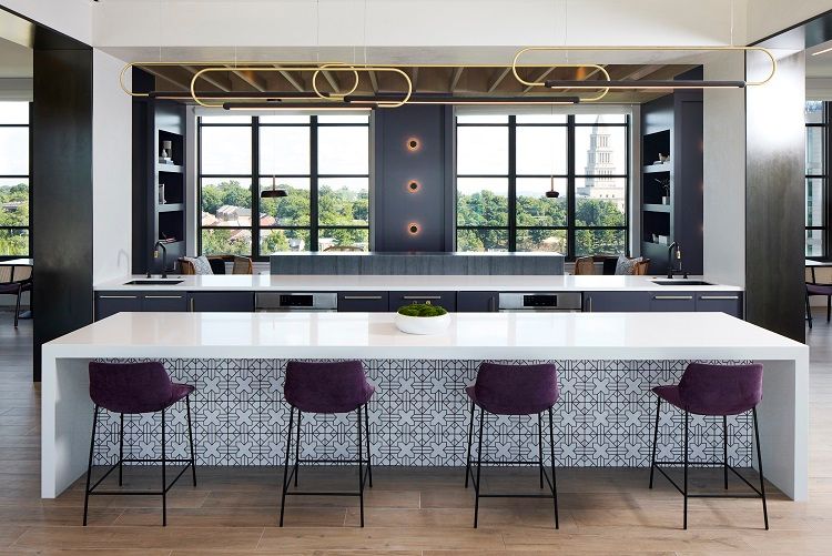 Modern kitchen bar with a white countertop, purple stools, and large windows.