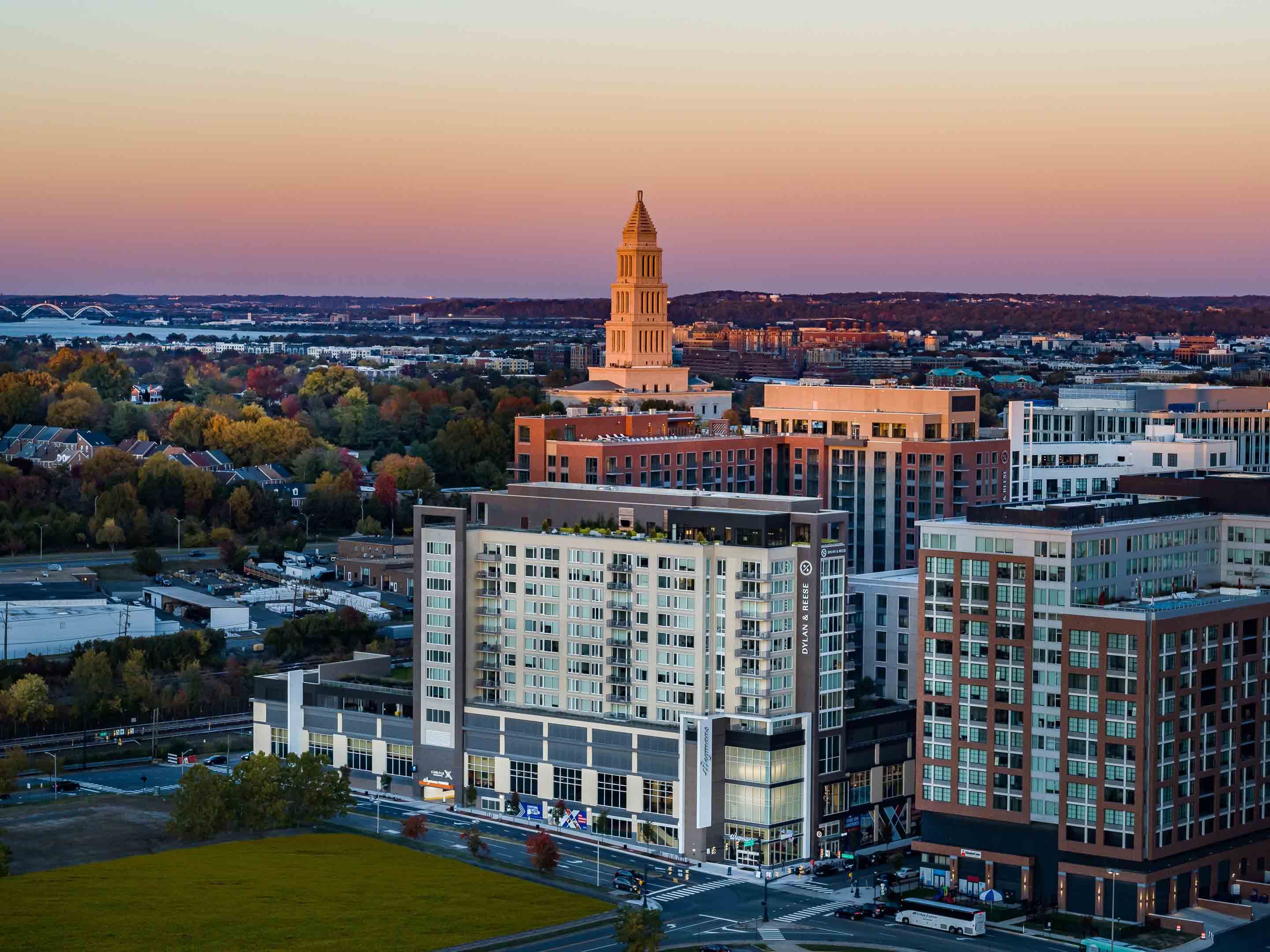 A skyline view at sunset featuring modern buildings and a tower in the background.