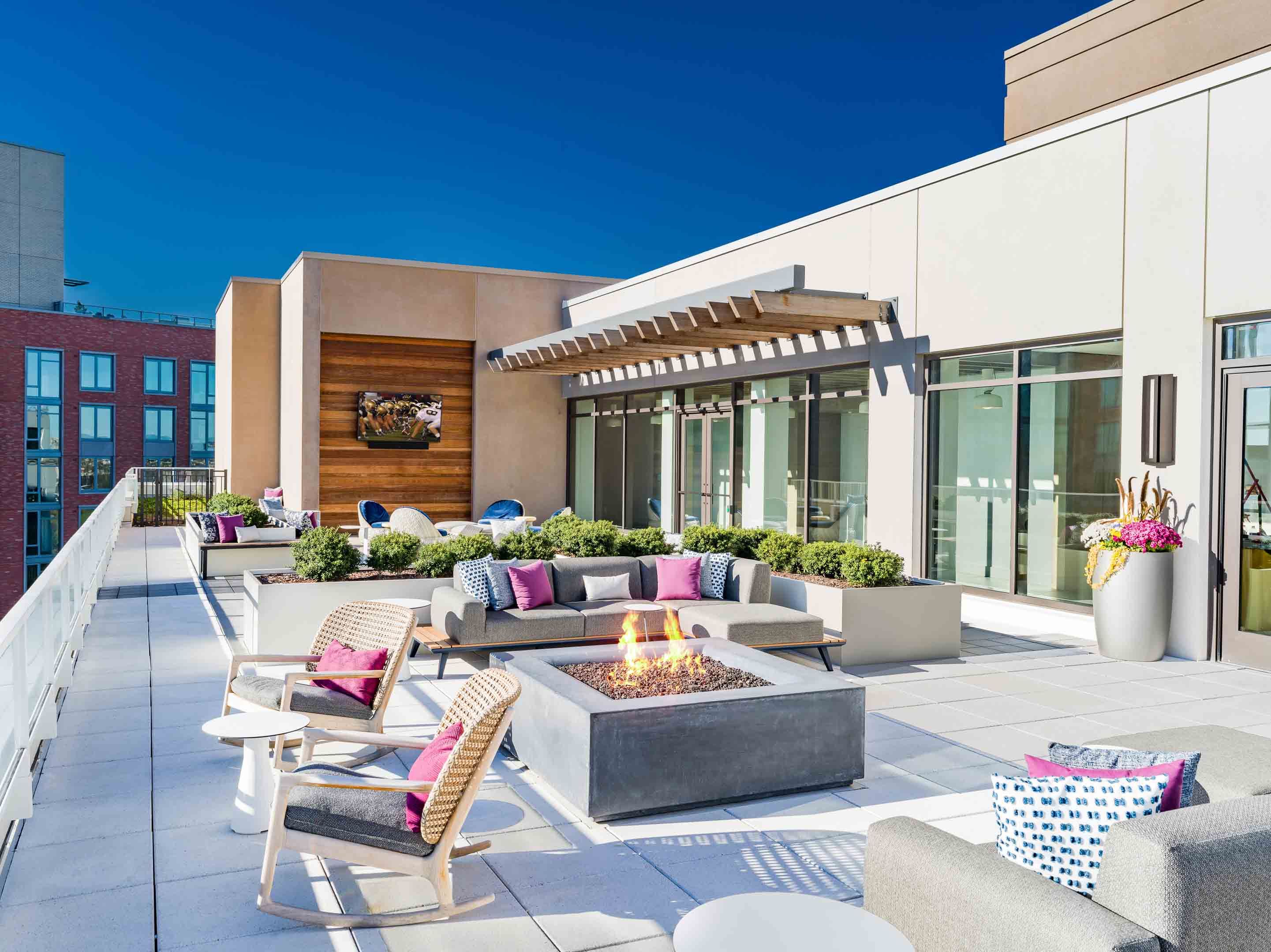 Rooftop lounge with modern seating and a fire pit against a clear blue sky.
