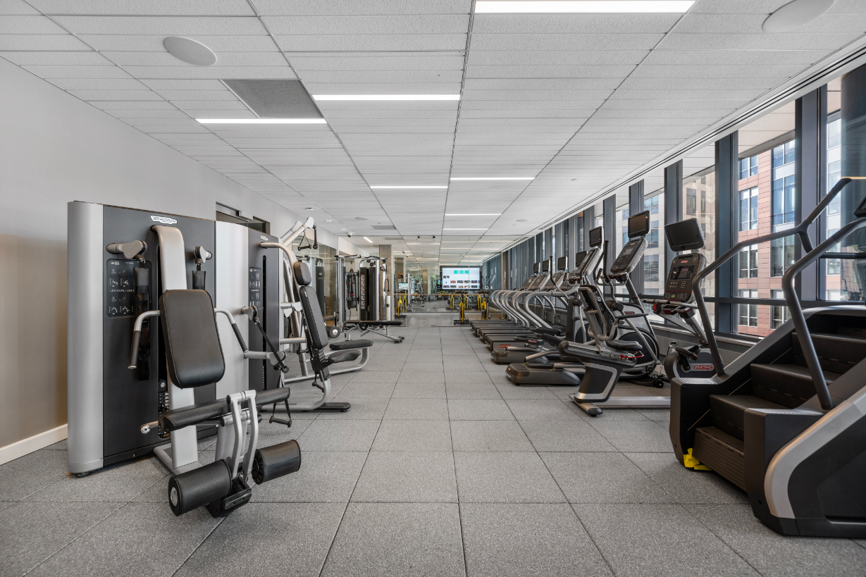 Modern gym interior with various exercise machines and bright windows.