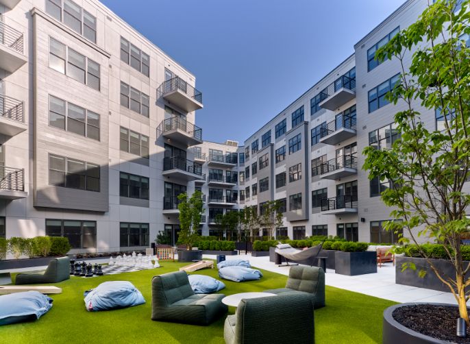 Modern apartment complex courtyard with green lawn and lounge seating.