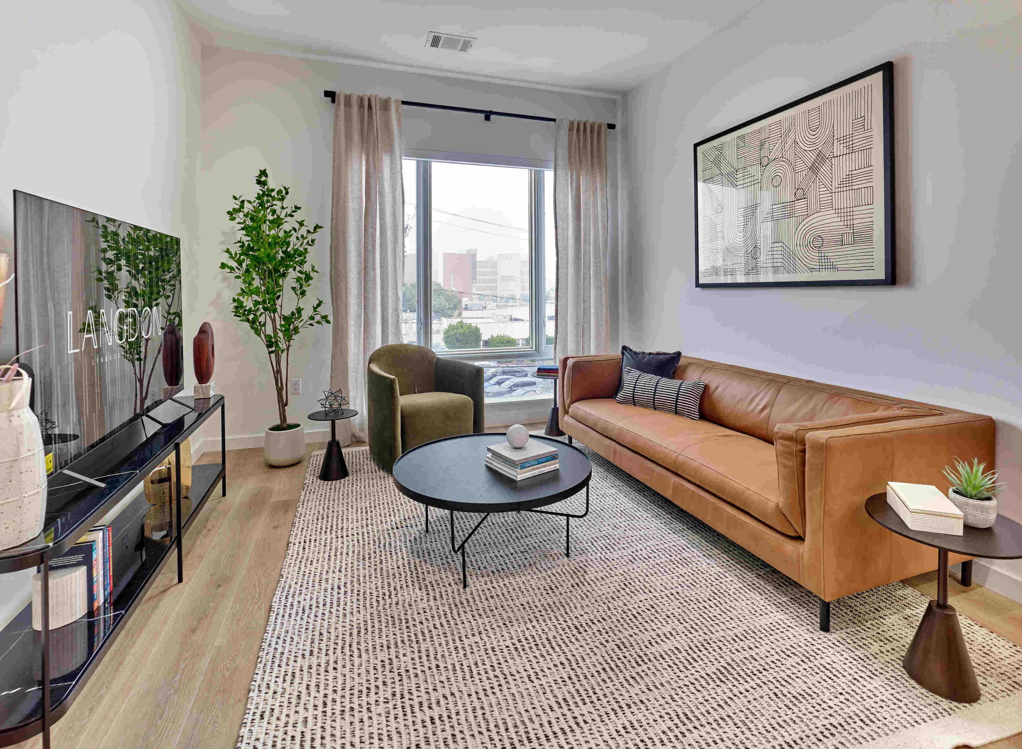 Modern living room with a brown sofa, green chair, plants, and a round coffee table by a window.