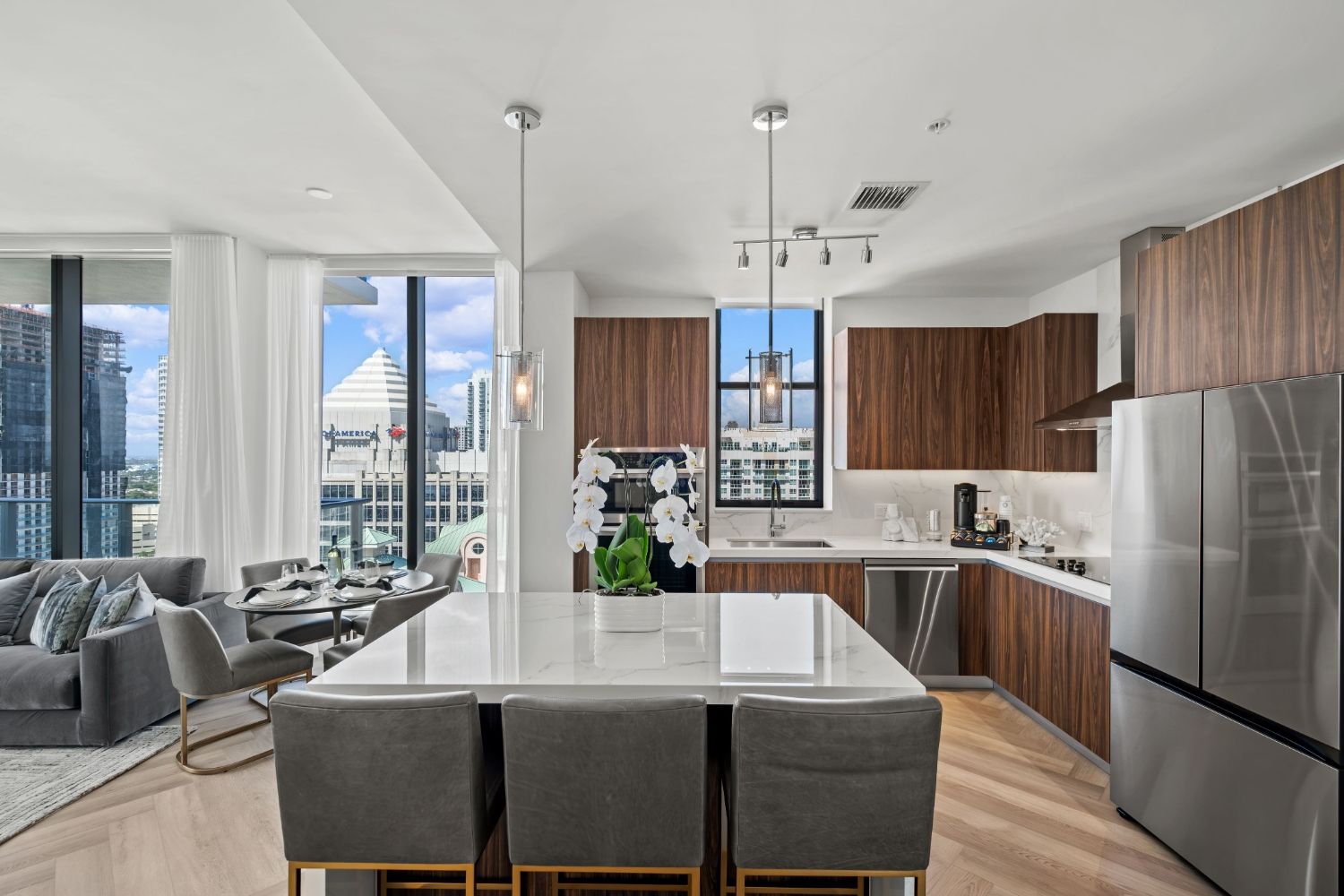 Modern kitchen with marble island, stainless appliances, and large windows showing city views.