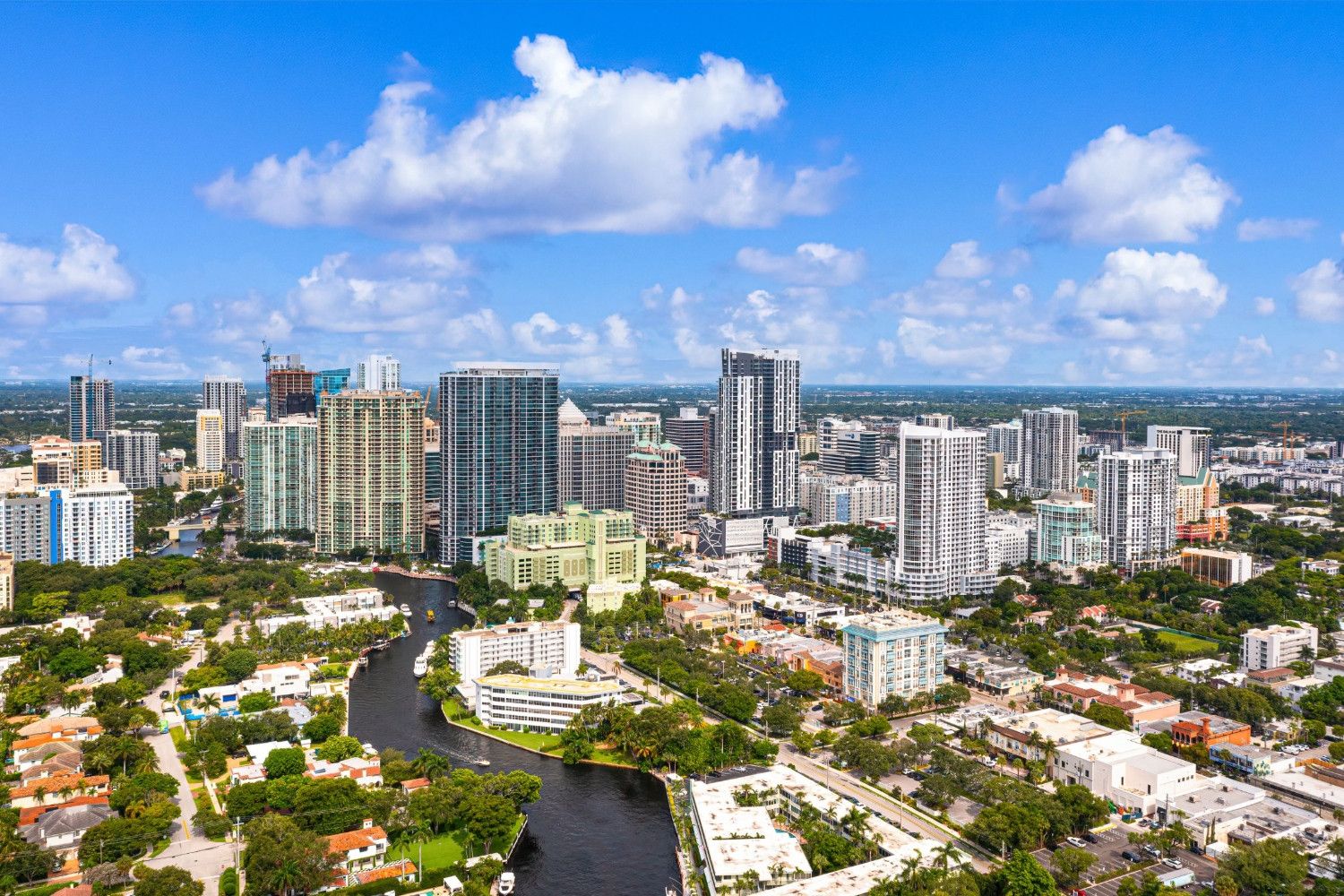 Aerial view of a modern city with skyscrapers and a river running through it under blue skies.