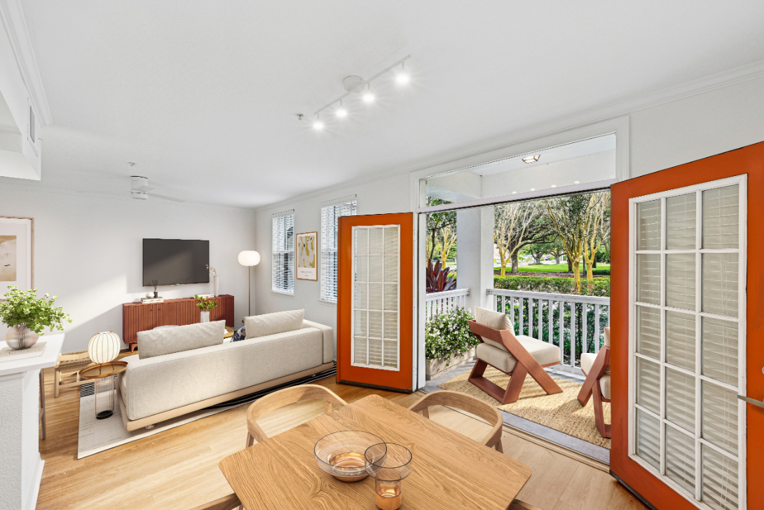 Bright living room with open doors leading to a balcony and green outdoor view.