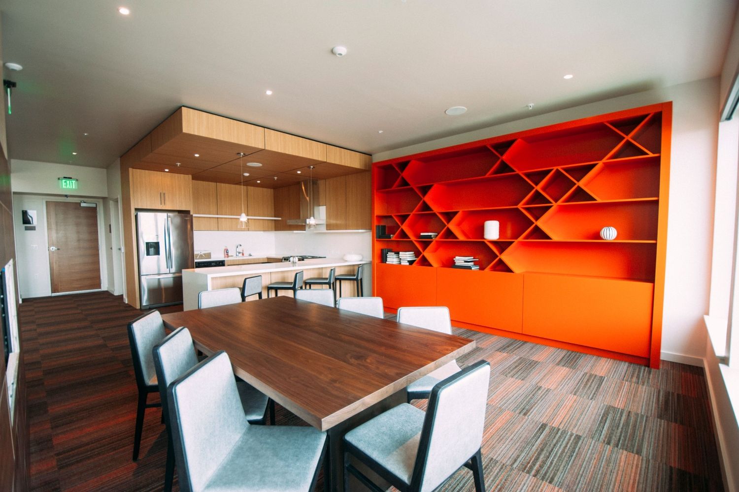 Modern kitchen with wooden cabinets, an orange bookshelf, and a dining table.