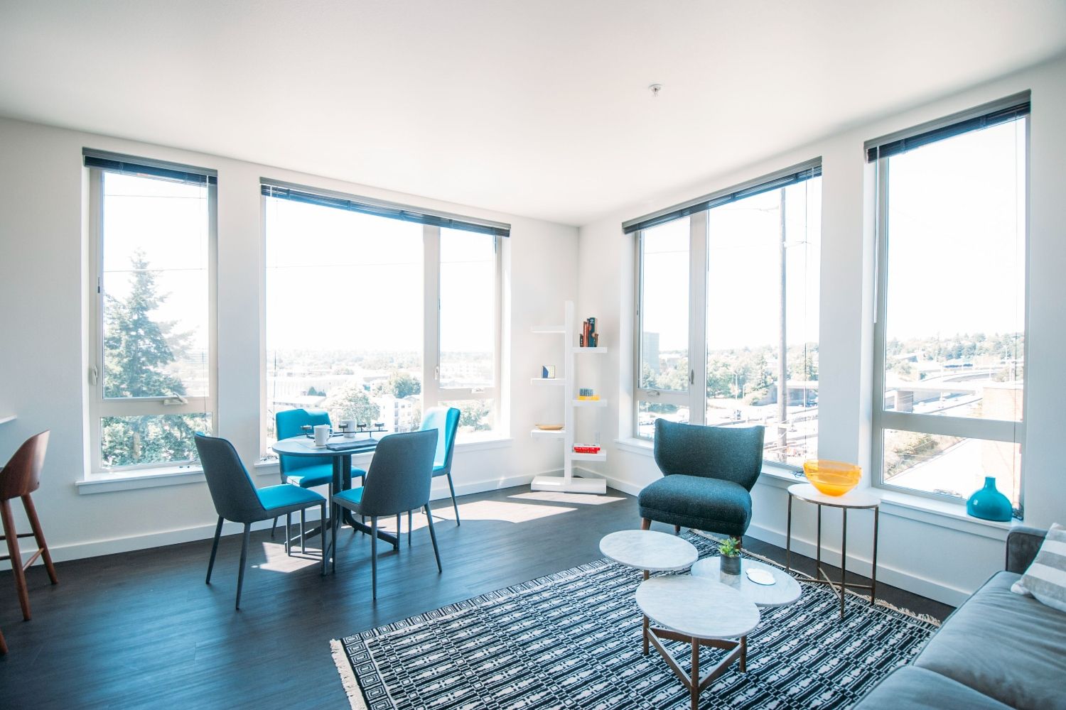 Modern living room with large windows, minimalist furniture, and city views.